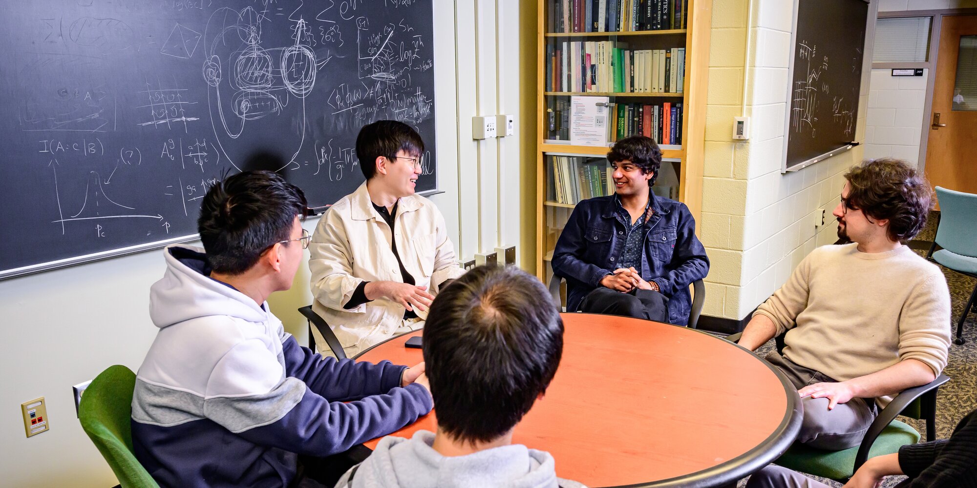 Members of the Lee group talking around a table in front of a chalkboard